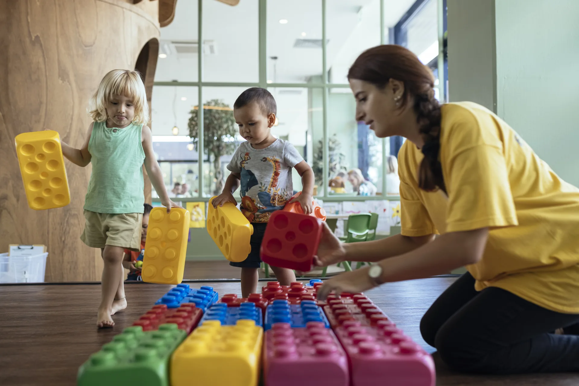 Bambini giocano con costruzioni colorate insieme a un’animatrice Benvenuto